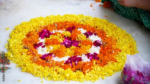 young indian woman sitting cross legged placing flower petal patterns on teh ground making a rangoli pookalam for the hindu festival of diwali, onam, bihu or a wedding with marigold jasmine flowers photo