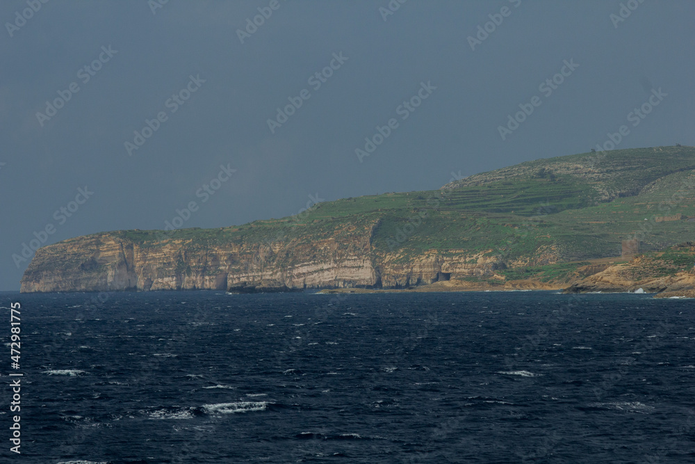 View to town from water sailing towards coast with old buildings in Malta, Gozo