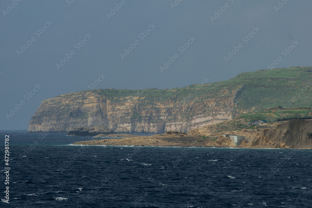 View to town from water sailing towards coast with old buildings in Malta, Gozo