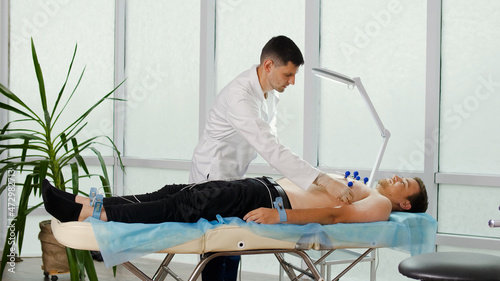 Electrocardiogram Procedure for Diagnosing Heart Disease. A Cardiologist Puts Electrodes on the Bare Chest of a Young Man Lying on the Couch To Take an Electrocardiogram in the Clinic'S Office.