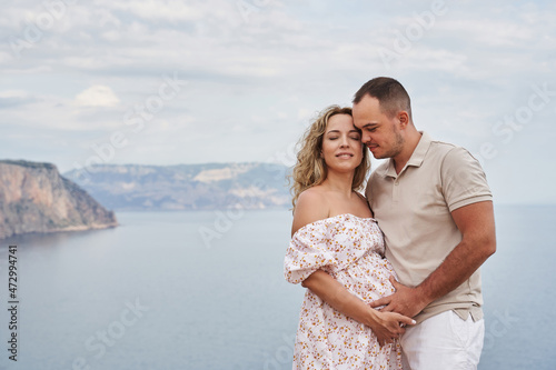 beautiful couple on the background of a beautiful seascape. a man gently holds a pregnant woman by the stomach. smiling woman