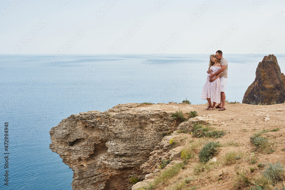 beautiful couple on the background of a beautiful seascape. a man hugs a pregnant woman from behind.