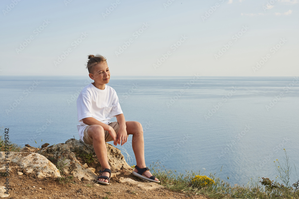 a boy sits on a stone against the backdrop of the endless sea horizon. dreamer, travel dreams. beautiful landscape