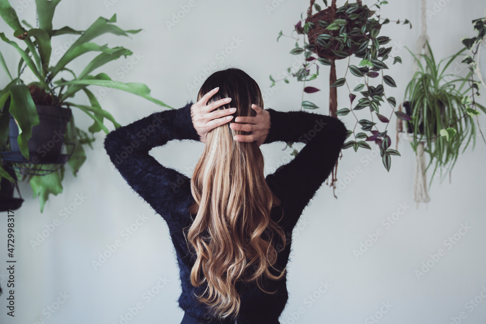 Fototapeta premium 植物に囲まれた室内で手で髪を束ねる女性のポートレート