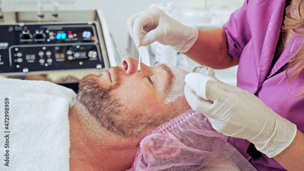 Cosmetologist applies a medical on male face. Adult man in a spa salon on cosmetic procedures for facial care. White middle-aged man getting beauty treatment therapy. Cosmetologist applies a medical on male face. Adult man in a spa salon on cosmetic procedures for facial care. White middle-aged man getting beauty treatment therapy.