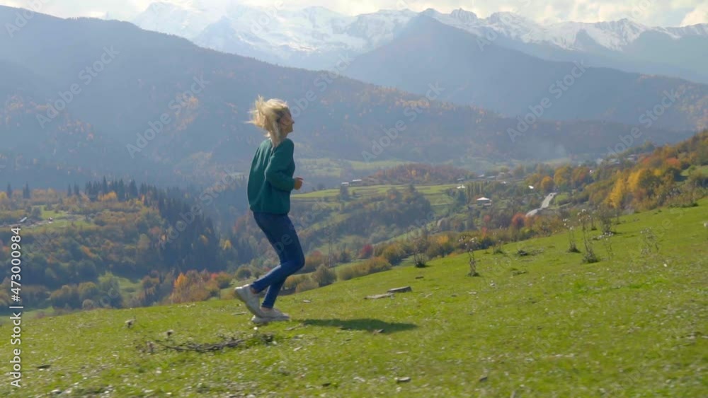 camera follows young beautiful woman who runs uphill on slope against background of valley of mountains. Autumn. runs all happy and joyful, inspired by landscape. Blonde in green sweater And jeans. camera follows young beautiful woman who runs uphill on slope against background of valley of mountains. Autumn. runs all happy and joyful, inspired by landscape. Blonde in green sweater And jeans.