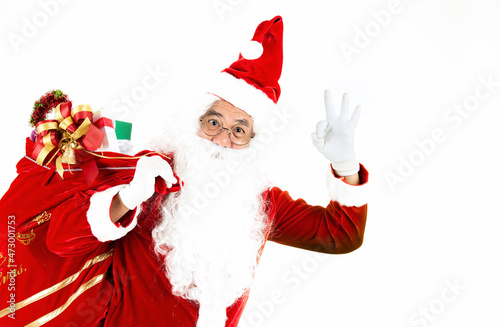 Old senior man with white hair and long beard wearing santa claus costume holding and make finger ok sign with bag of presents and for surprised in christmas eve. Santa claus making a silence gesture.