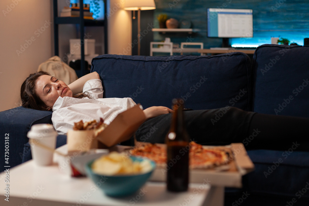 Person sleeping on sofa after drinking beer and eating home delivery pizza in front of television in living room. Tired woman falling asleep couch after large fast food takeout meal. Person sleeping on sofa after drinking beer and eating home delivery pizza in front of television in living room. Tired woman falling asleep couch after large fast food takeout meal.