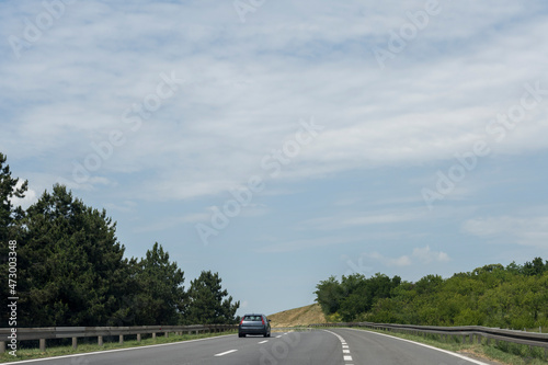 The blue car is driving on the new highway. Sunny summer day with blue skies and white clouds.