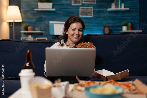 Photography Portrait of smiling woman watching online television sitcom on laptop eating a home delivery burger for dinner