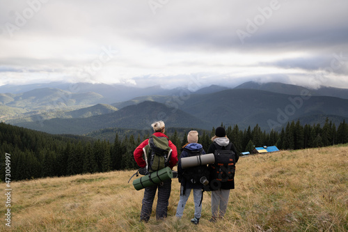 Group of tourists with backpacks in the mountains, back view, mountain range in the clouds, travel and tourism in the Alps or Caucasus mountains. © mtrlin