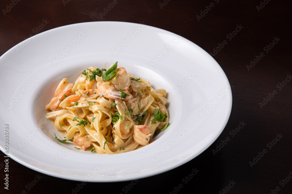 Italian pasta with prawns chili pepper and greens. Italian food, white dish, dark background