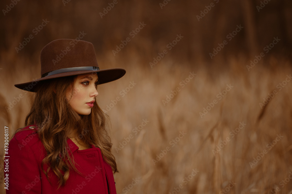 Elegant beautiful woman wearing trendy brown hat, red marsala color classic coat posing in nature. Outdoor autumn fashion close up profile portrait. Copy, empty space for text