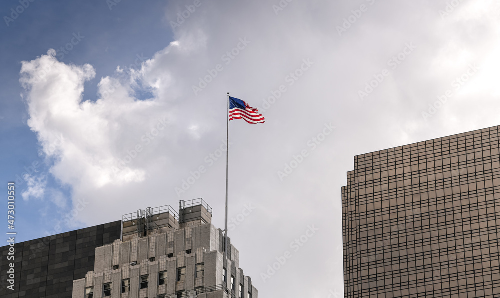 The national flag of United States of America winding between the tall skyscraper buildings from Manhattan, New York. Patriotism symbol..