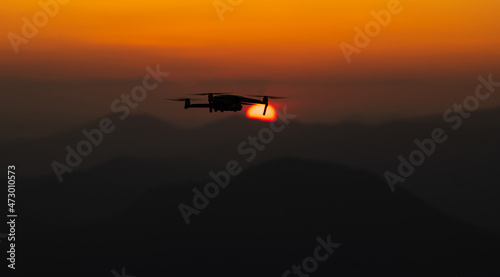 Drone in flight. Silhouette of an UAV quadcopter flying in front of the sun during sunset on top of the mountains. Drones industry.