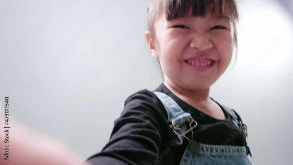 Happy little Asian girl using a smartphone for video call, waving hand and speaking and talking with a smile greeting teacher and classmates. Happy little Asian girl using a smartphone for video call, waving hand and speaking and talking with a smile greeting teacher and classmates.