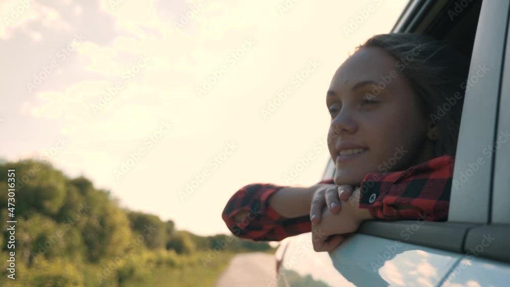young girl looks out of car window, wind in hair.Smiling girl travels by car, hanging her head from car through open window, enjoying freedom of breeze in hair.Traveling through countryside of young. young girl looks out of car window, wind in hair.Smiling girl travels by car, hanging her head from car through open window, enjoying freedom of breeze in hair.Traveling through countryside of young.