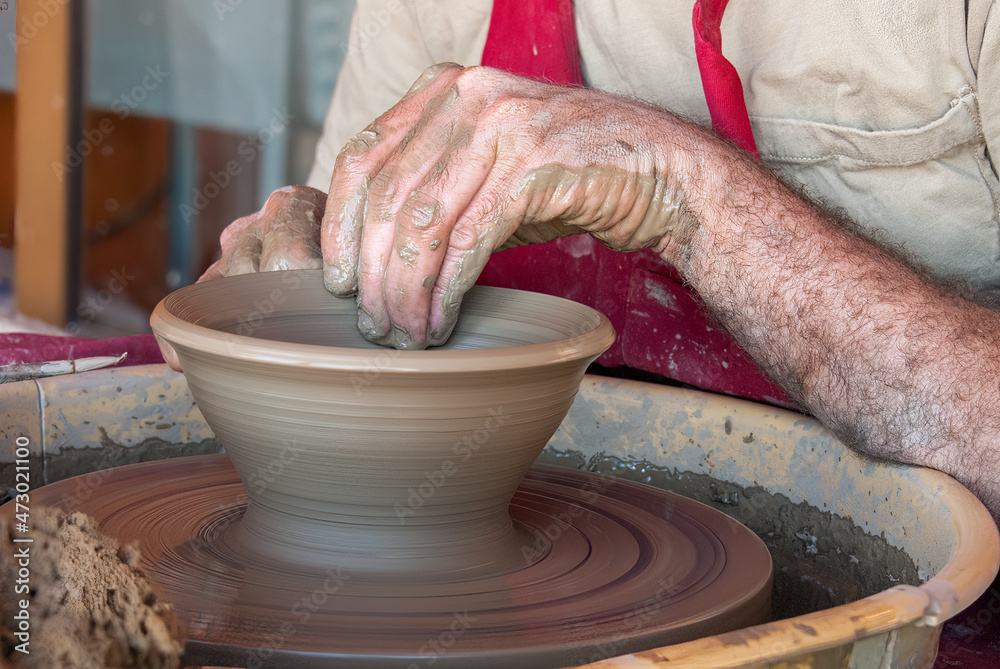 Hands of a caucasian  potter shaping a clay pot on a fast rotating potters wheel.