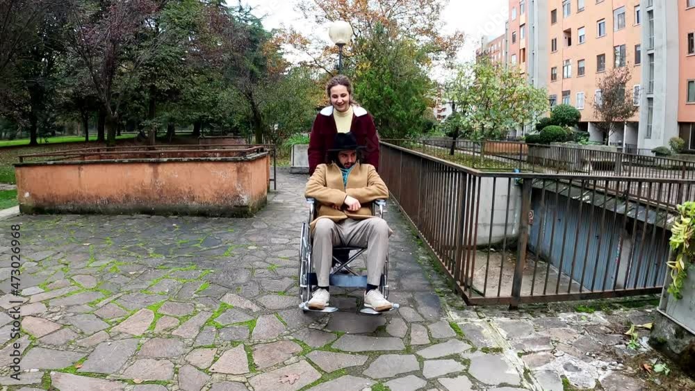 living with a disability - young man who is paralyzed accompanied by his girlfriend pushing his wheelchair living with a disability - young man who is paralyzed accompanied by his girlfriend pushing his wheelchair