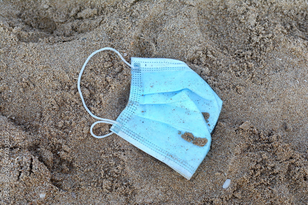 Old anti virus mask thrown on the beach sand. A blue disposable face mask found on the beach during COVID-19 pandemic. Old anti virus mask thrown on the beach sand. A blue disposable face mask found on the beach during COVID-19 pandemic.