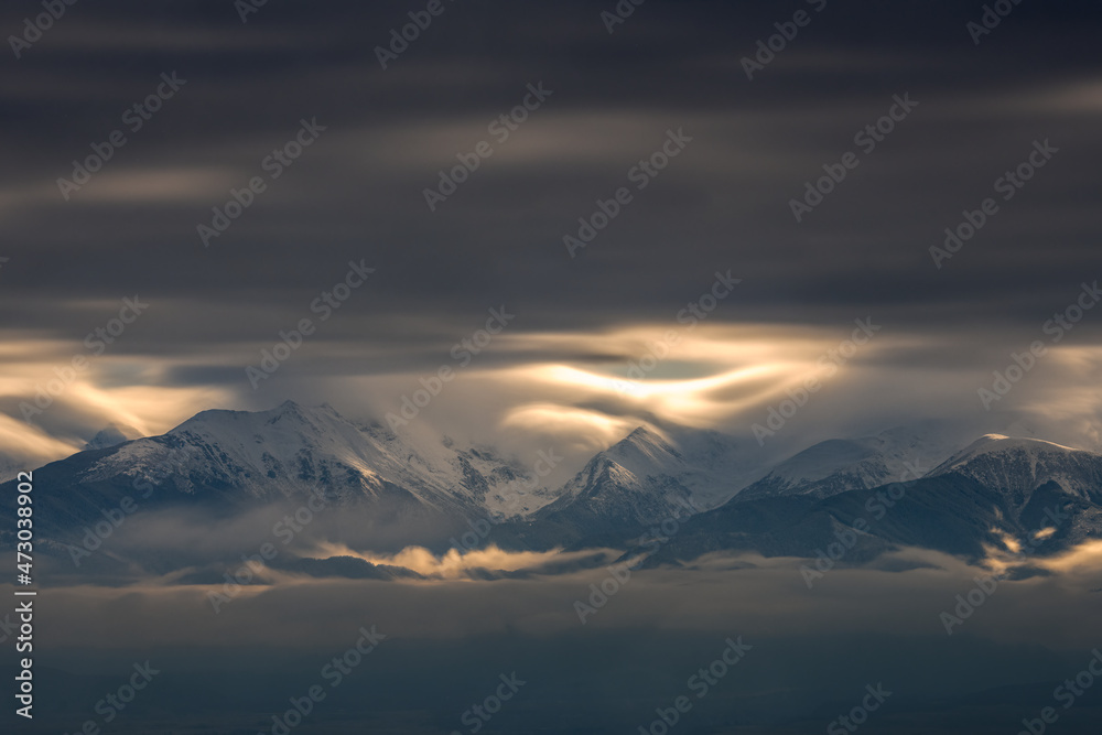 Dramatic sky with clouds over the mountains covered in snow