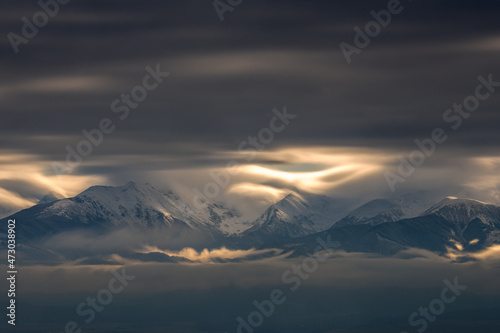 Dramatic sky with clouds over the mountains covered in snow