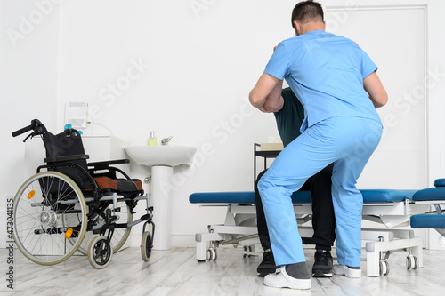 Male Physiotherapist helping a patient with a disability who uses a wheelchair, to get up at rehabilitation hospital. High quality photo. photo