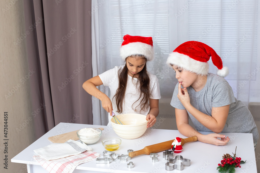 two Happy children, brother and sister, in red caps, prepare Christmas cookies in the kitchen