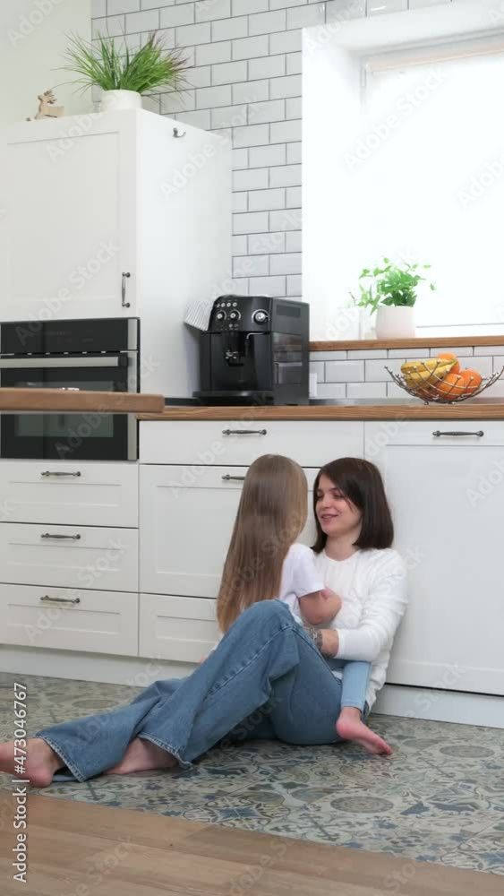 A mother with a blonde daughter sits and talks on the kitchen floor A mother with a blonde daughter sits and talks on the kitchen floor