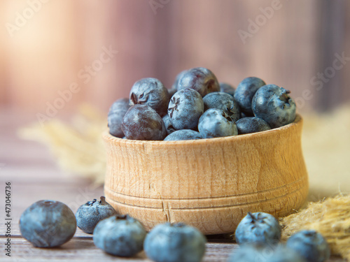 Freshly picked blueberries in a wooden bowl on a wooden background. Healthy food and nutrition. Place for text.
