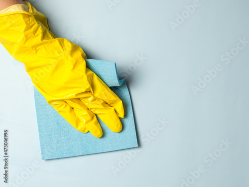 A hand in a yellow rubber glove holds a cleaning sponge in soapy foam on a blue background. House cleaning concept, cleaning service