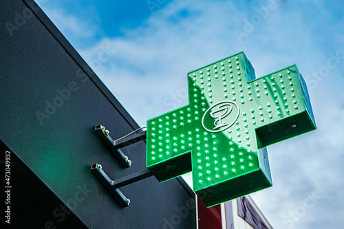 Neon medical bright shining glowing green illuminated urban pharmacy drug store cross sign light bulbs outside street night evening on building in city during coronavirus pandemic quarantine