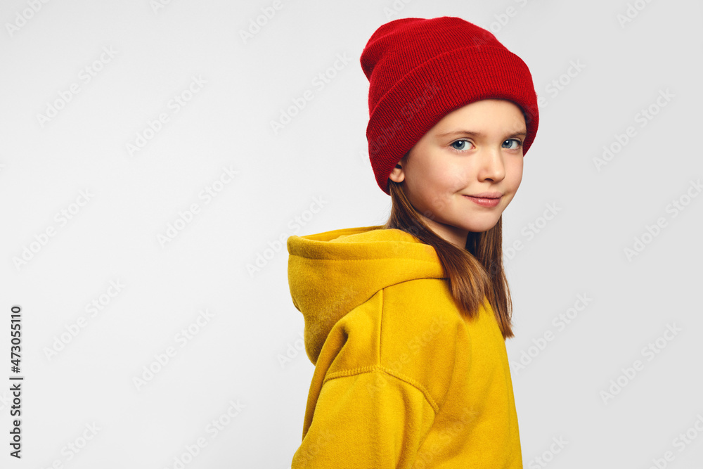 Adorable hipster kid with pleasant smile, wears yellow hoodie and red hat, stands against white background, copy space for your advertisement Adorable hipster kid with pleasant smile, wears yellow hoodie and red hat, stands against white background, copy space for your advertisement