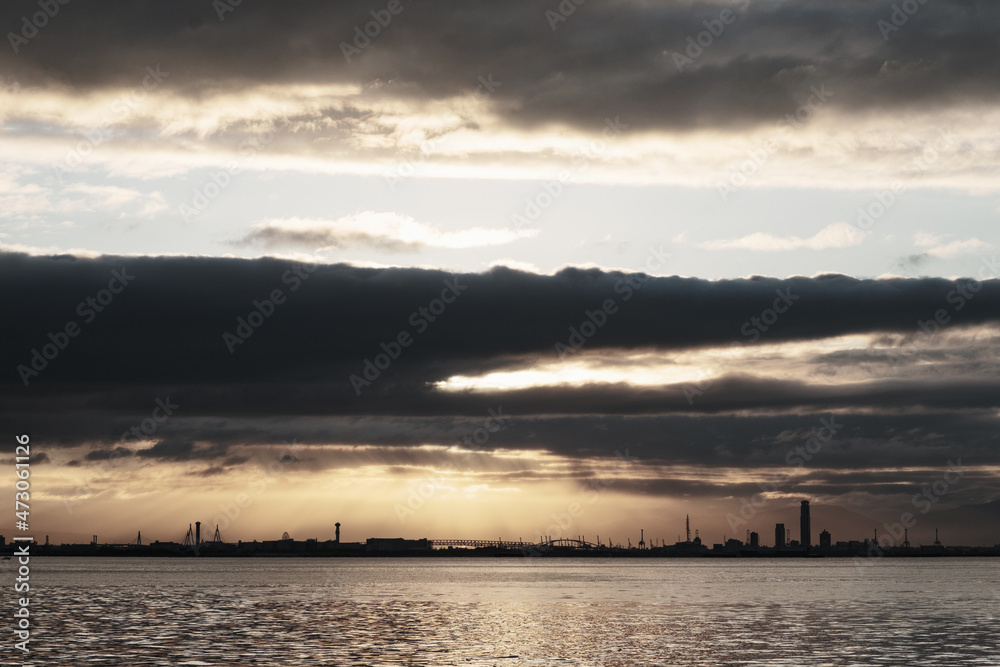 Obraz premium 兵庫県芦屋市芦屋浜の夜明け。日の出とともに あたりはオレンジ色に染まる。大阪湾を隔てて大阪市街地のビルがシルエットで浮かぶ