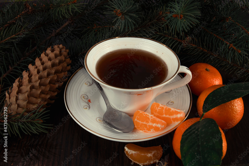 Mug of tea with tangerines and Christmas tree branches. Dark background.