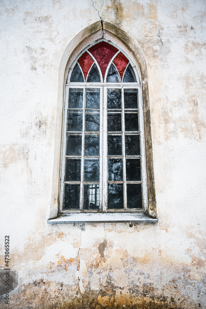 Large window with stained glass and old, peeled wall. Old historical lutheran church, Barbele, Latvia