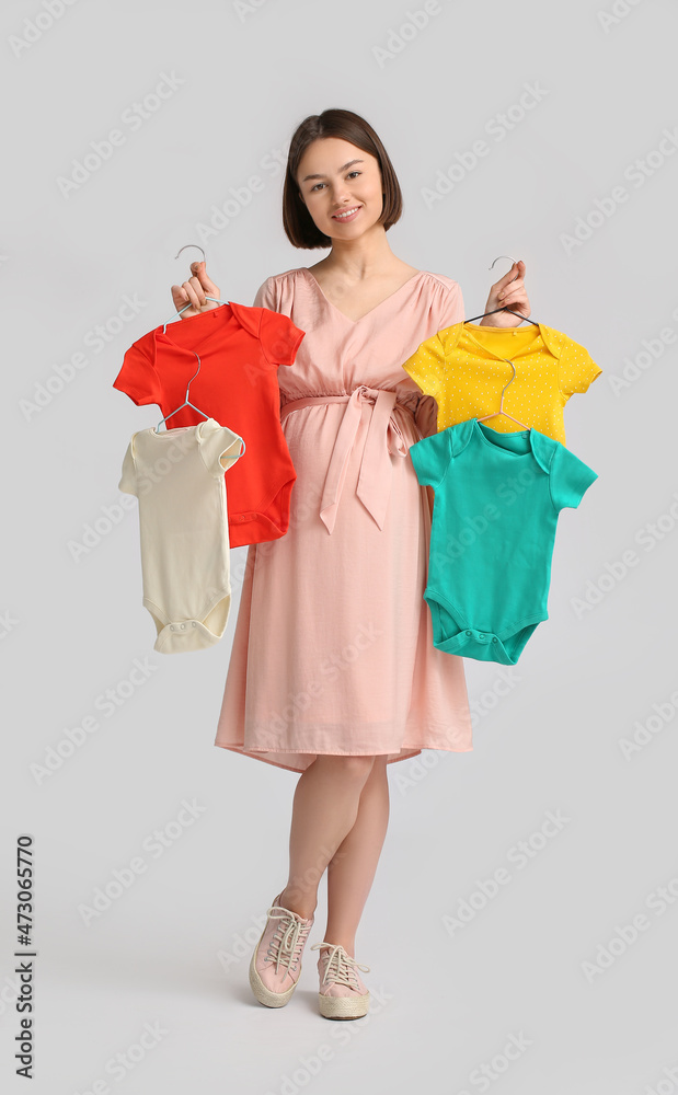 Young pregnant woman with baby bodysuits on light background Young pregnant woman with baby bodysuits on light background