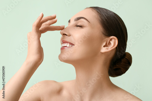 Young woman with healthy skin touching nose on color background photo