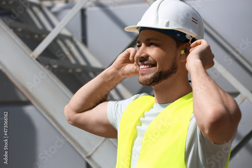 Male builder putting ear plugs outdoors photo