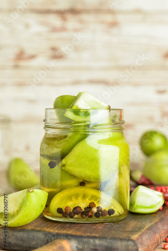 Jar with canned green tomatoes on table