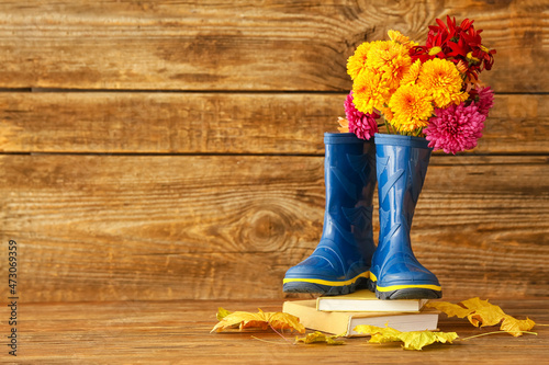Pair of rubber boots, chrysanthemum flowers and autumn leaves on wooden background