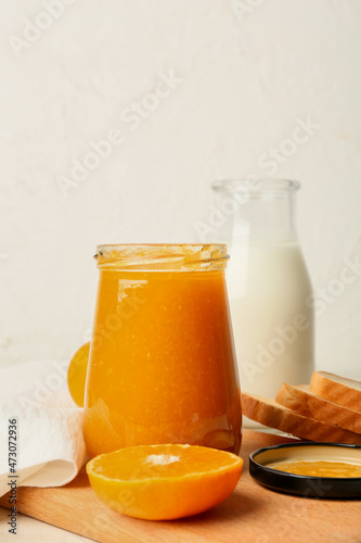 Jar of tasty tangerine jam and milk on light background