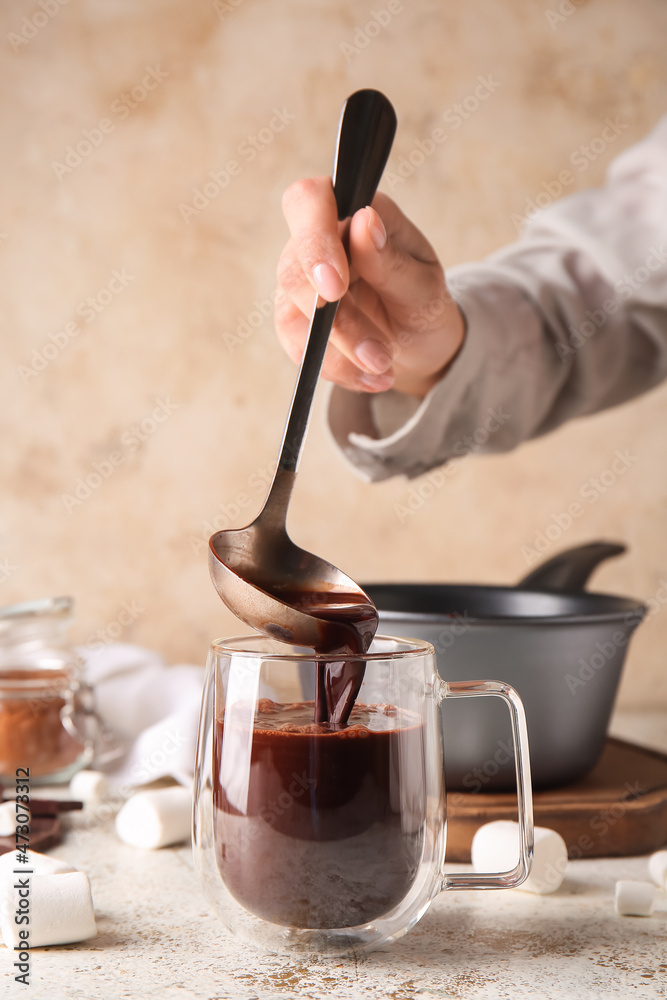 Woman pouring tasty hot chocolate into glass cup on light background Woman pouring tasty hot chocolate into glass cup on light background