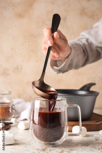 Woman pouring tasty hot chocolate into glass cup on light background