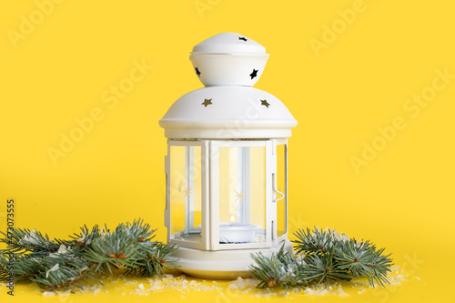 Beautiful Christmas lantern with burning candle and fir branches on yellow background