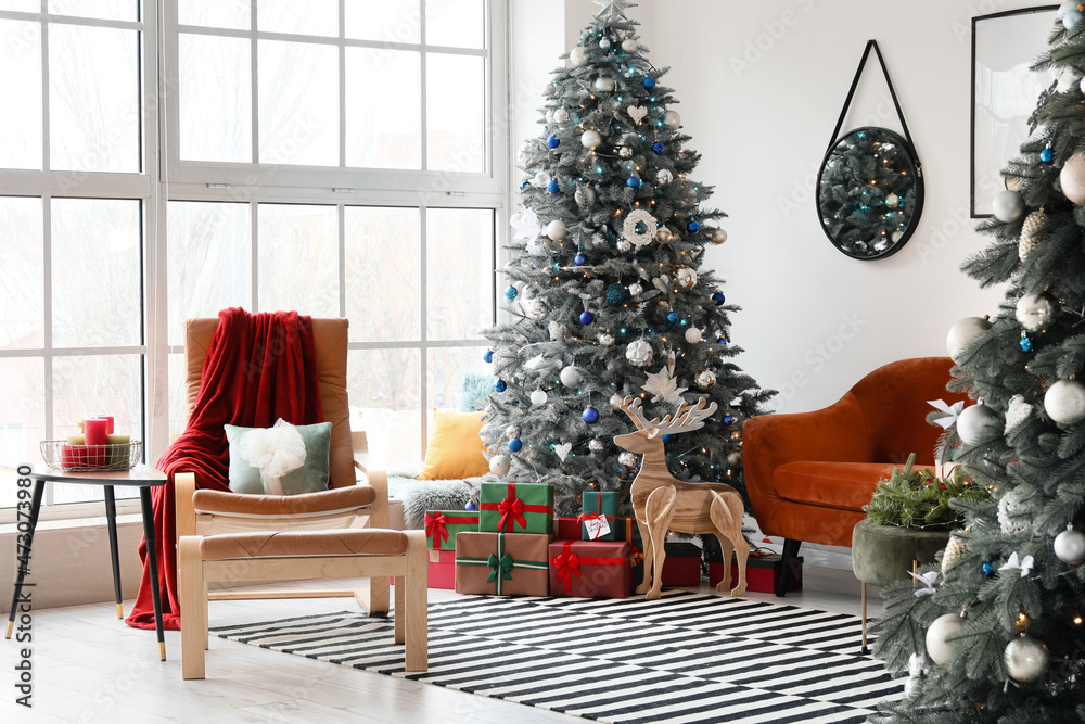 Comfy armchair, Christmas trees with gift boxes and wooden reindeer in living room