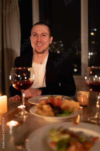 valentine s day dinner  portrait of a man at a festive table with red wine and candles  romantic home date  the guy prepared a surprise for girlfriend