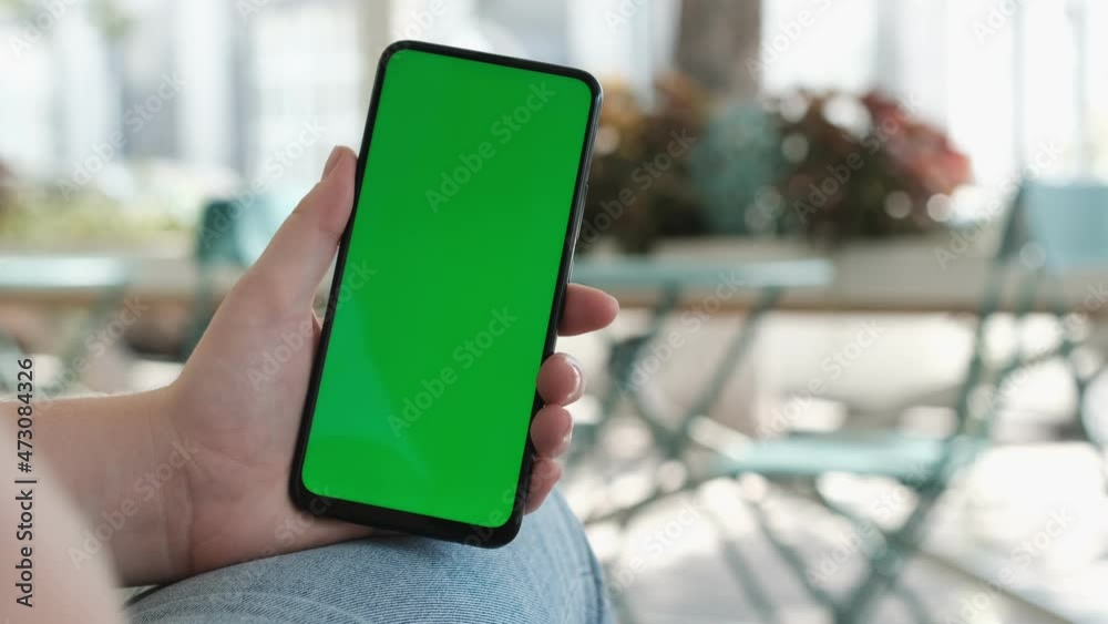 View of female hand holding and pressing on smartphone with mockup green screen in the restaurant european city. Concept of chroma key and greenscreen View of female hand holding and pressing on smartphone with mockup green screen in the restaurant european city. Concept of chroma key and greenscreen
