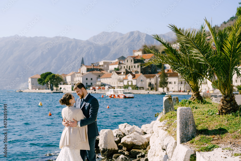 Bride and groom are hugging while standing on the stones off the coast of Perast. Montenegro