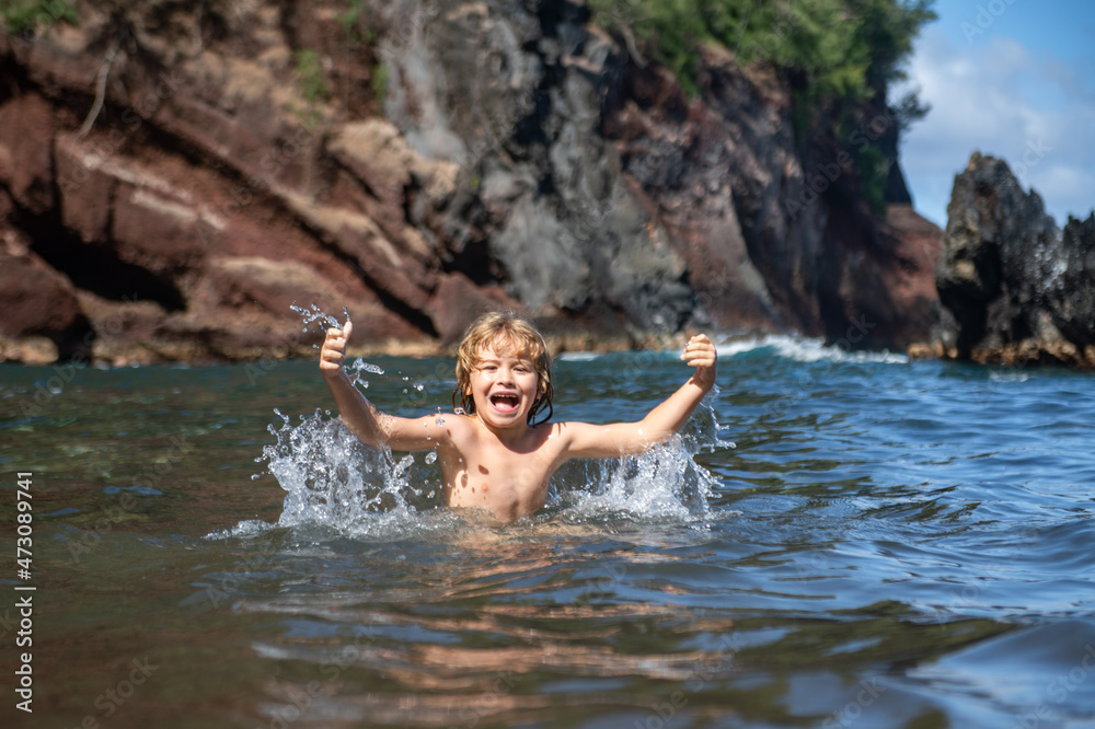 Fototapeta premium Child playing in ocean water. Kid jumping in the sea waves. Kids vacation on beach. Little excited boy swimming during summer holiday.